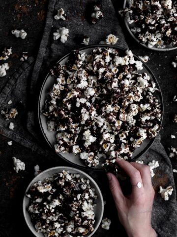 Reaching for some Chocolate Popcorn arranged in three bowls.