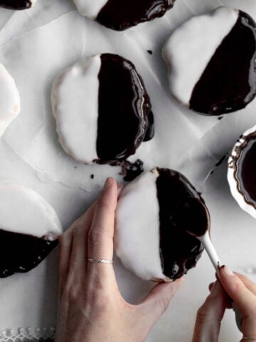 Hands add chocolate glaze to half of a gluten free black and white cookie.