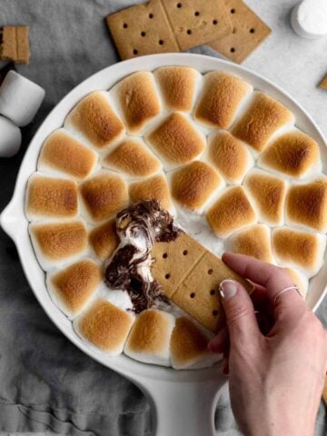 Scooping S’mores Dip from an array of toasted marshmallows with a cracker.