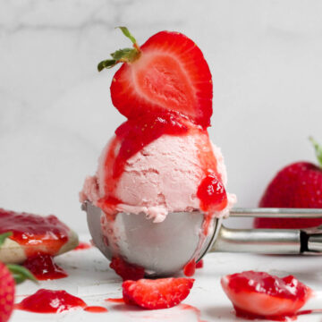 Scoop of luscious strawberry ice cream topped with strawberry syrup drizzle and a halved fresh strawberry.