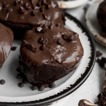 Gluten-free chocolate cinnamon rolls with shiny chocolate cream cheese frosting and chocolate chips on a plate.
