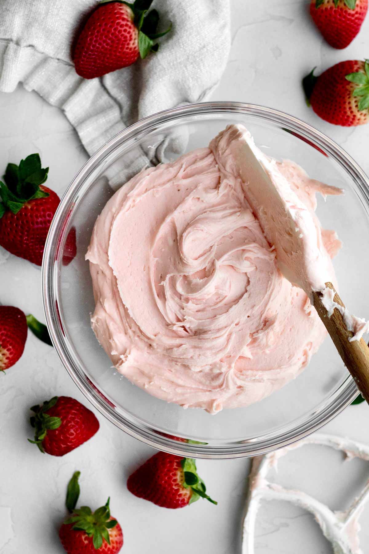A bowl of gluten free Vegan Strawberry Buttercream Frosting stirred by a spatula.