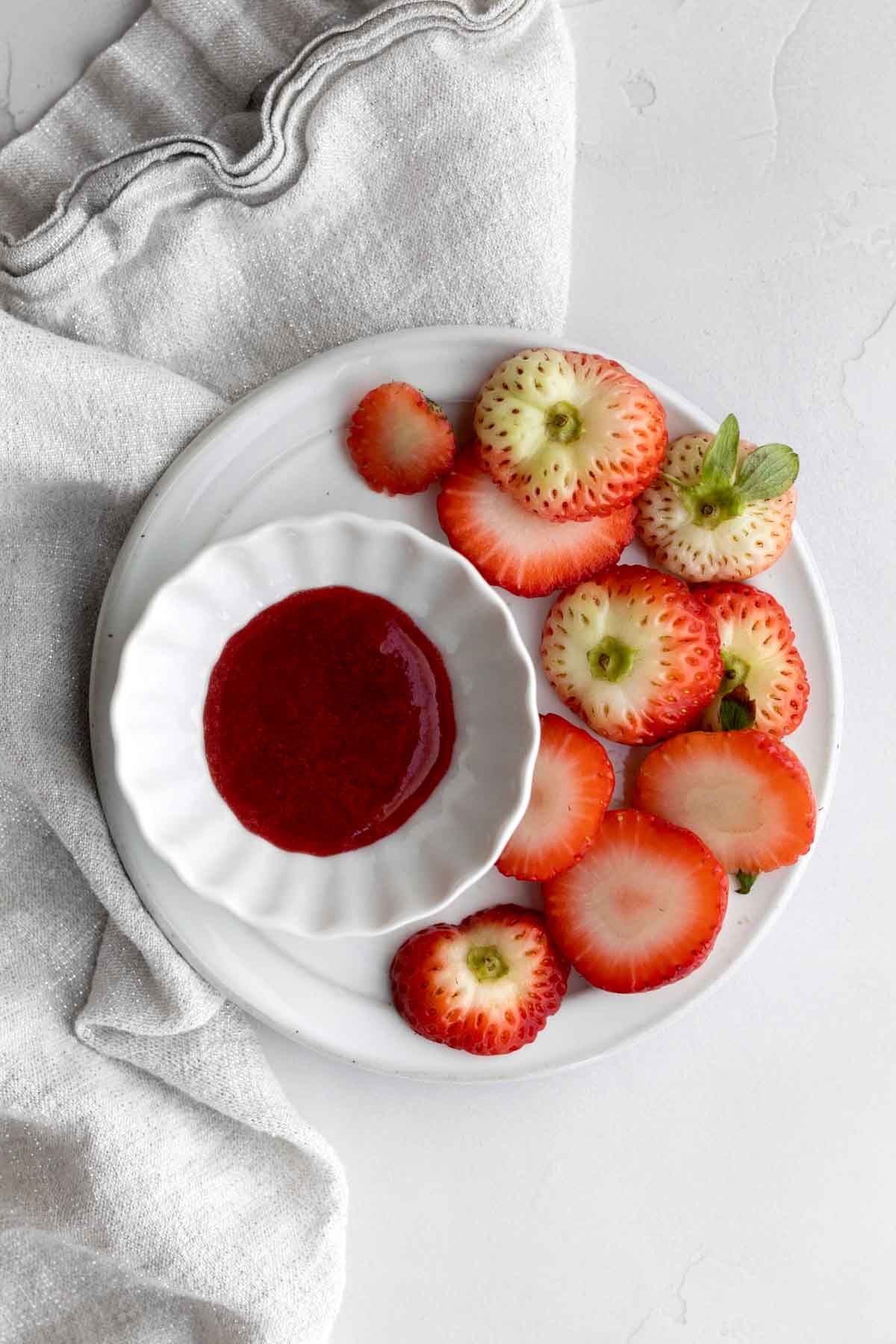 Strawberry liquid in a ramekin on a plate of cut strawberry tops.