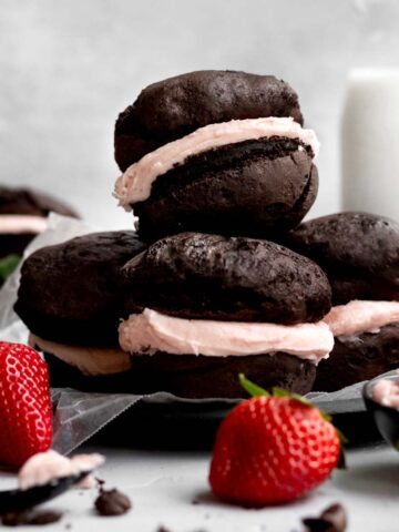 Four gluten free whoopee pies sit in a stack with strawberries.