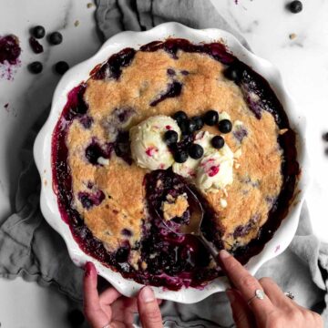 Scooping out servings of deliciously gooey gluten-free blueberry cobbler with ice cream.