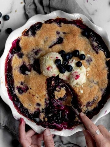 Scooping out servings of gluten free Blueberry Cobbler with ice cream.