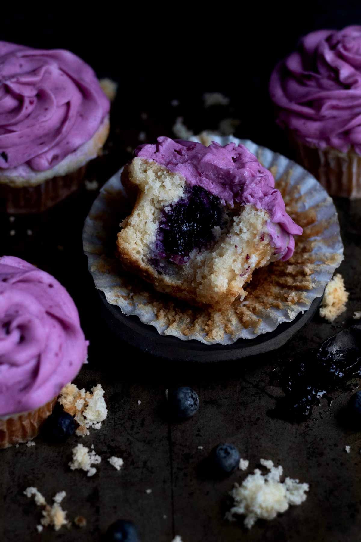 A bitten Blueberry Cupcake with the deep purple blueberry jam exposed.