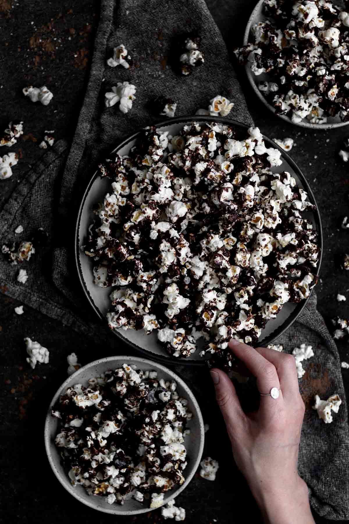 A hand picks a Chocolate Popcorn from a bowl.