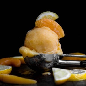 A scoop of Peach Sorbet topped with slices of lemon and peach.