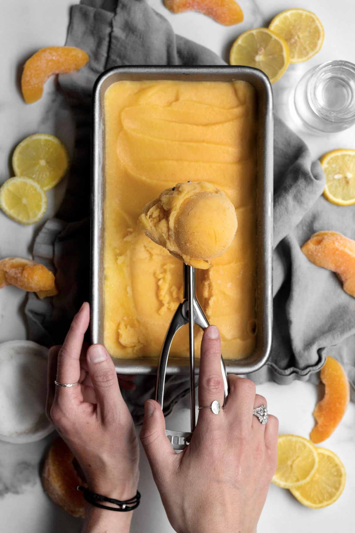 Scooping out orange Peach Sorbet from the pan.