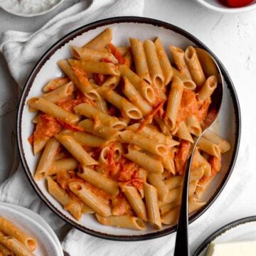 Gluten-free cherry tomato pasta with broken down tomatoes and creamy sauce in a rustic bowl.