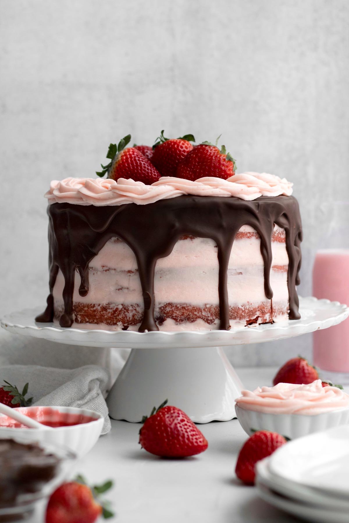 Strawberry Red Velvet Cake on a cake stand with extra strawberries.