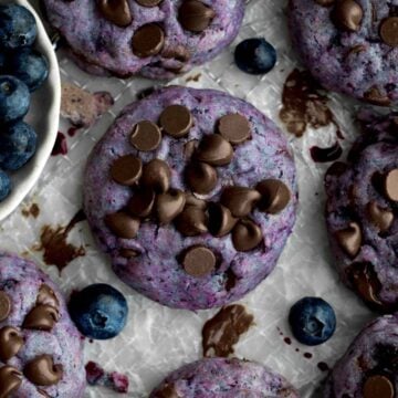 Gluten-free lavender and periwinkle chocolate chip blueberry cookie with slightly melted chocolate chips on parchment paper.