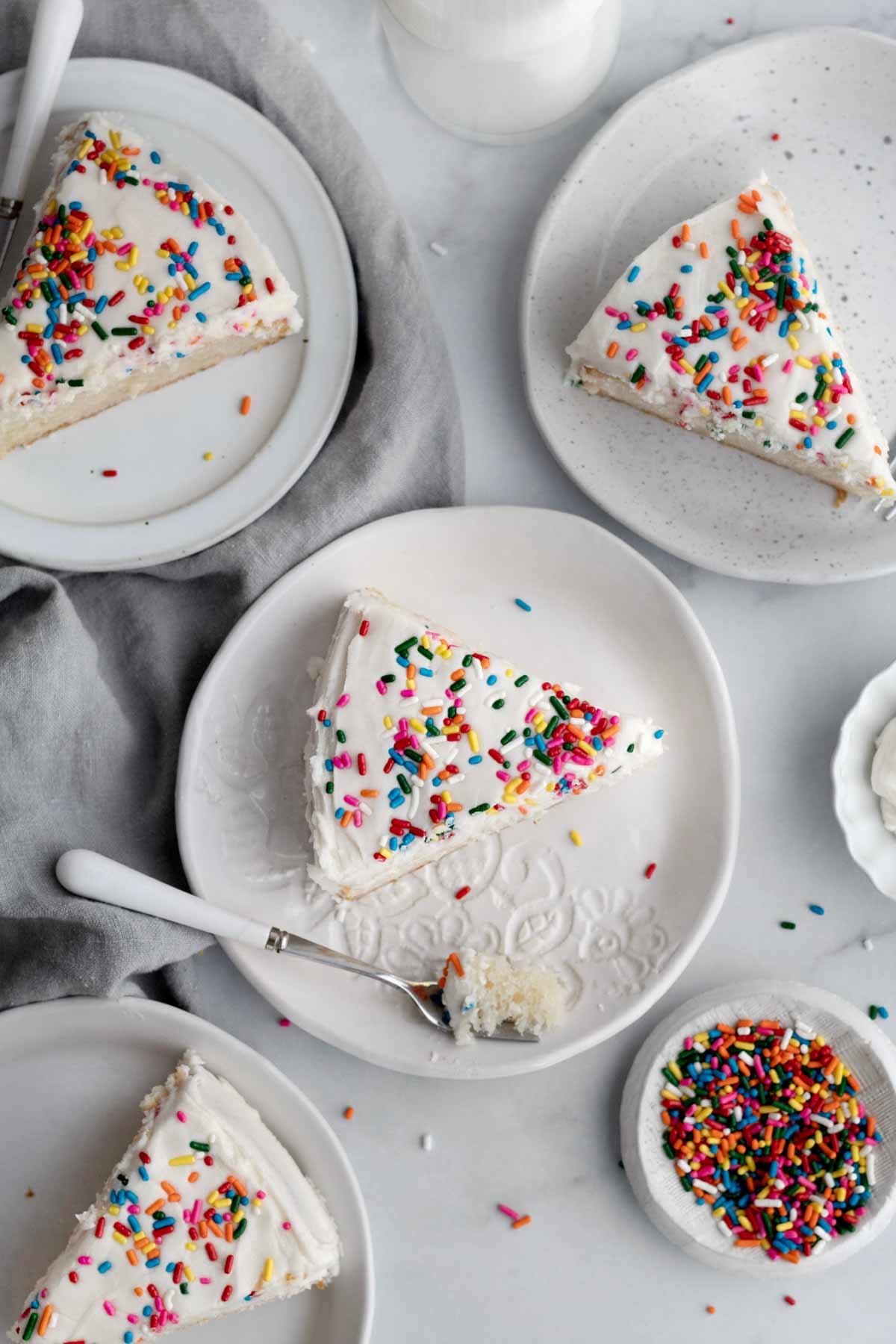 Four slices of cake on separate plates topped with rainbow sprinkles.