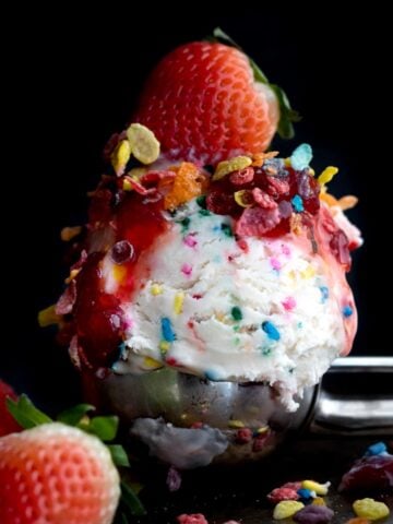 A scoop of sprinkle infused ice cream with Fruity Pebbles and a strawberry.