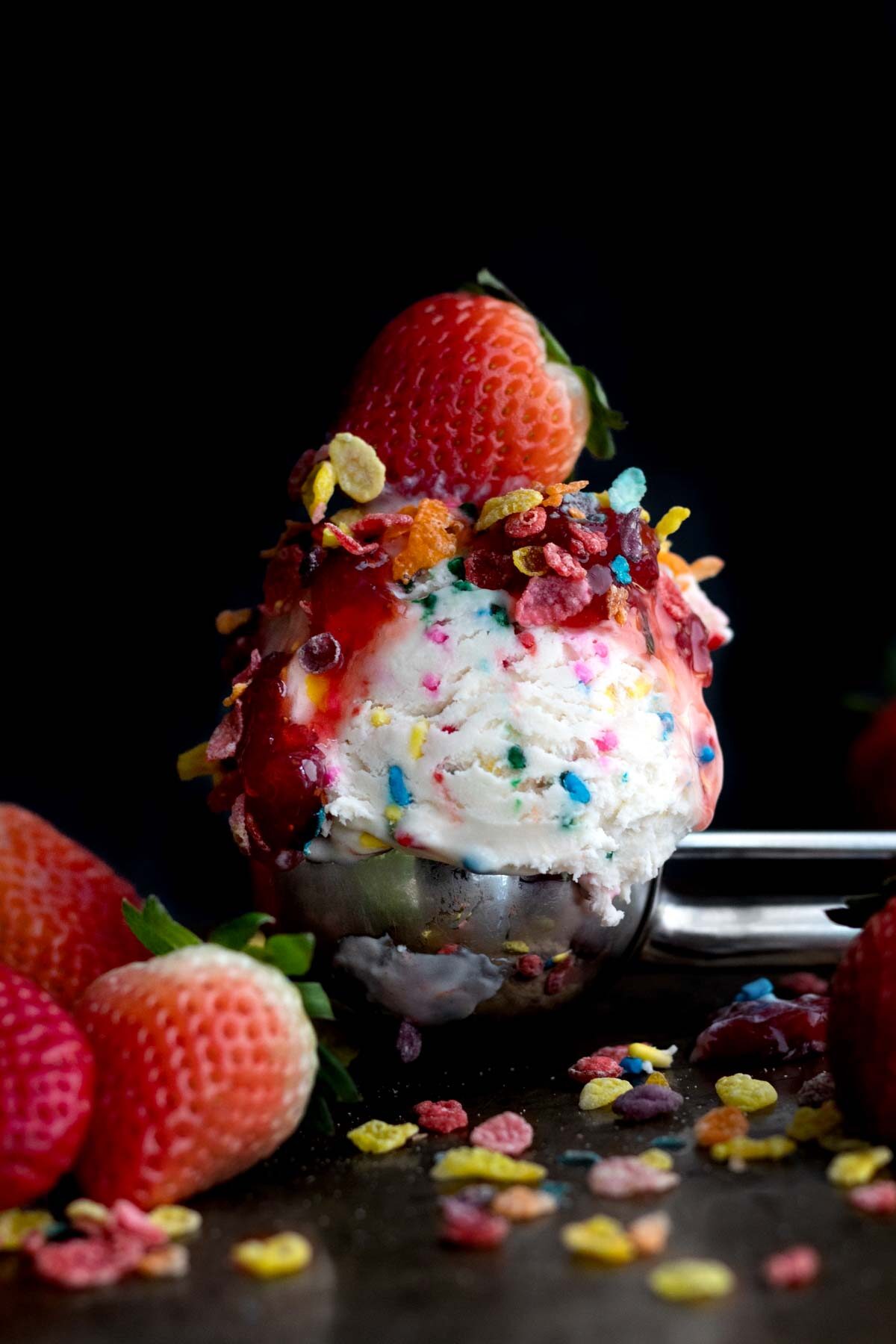 A scoop of sprinkle infused ice cream with Fruity Pebbles and a strawberry.