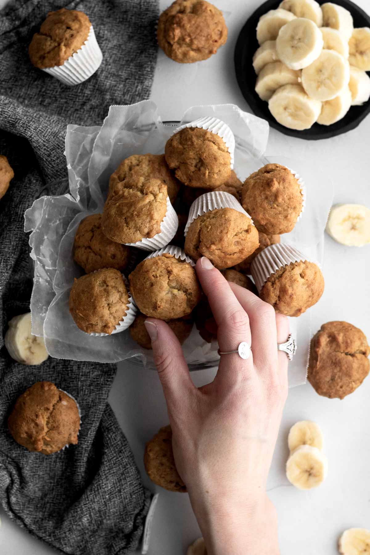 A hand grabs a banana muffin from the pile.