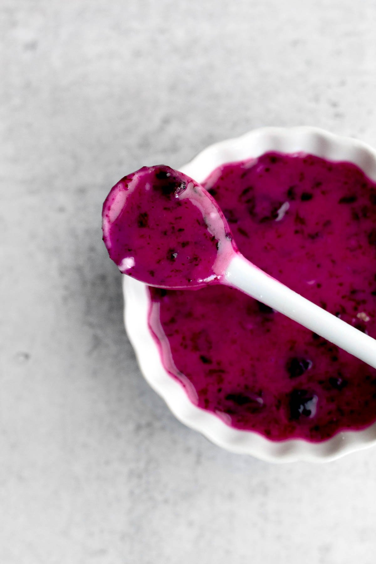 Hot pink blueberry glaze in a ramekin with a white spoon.