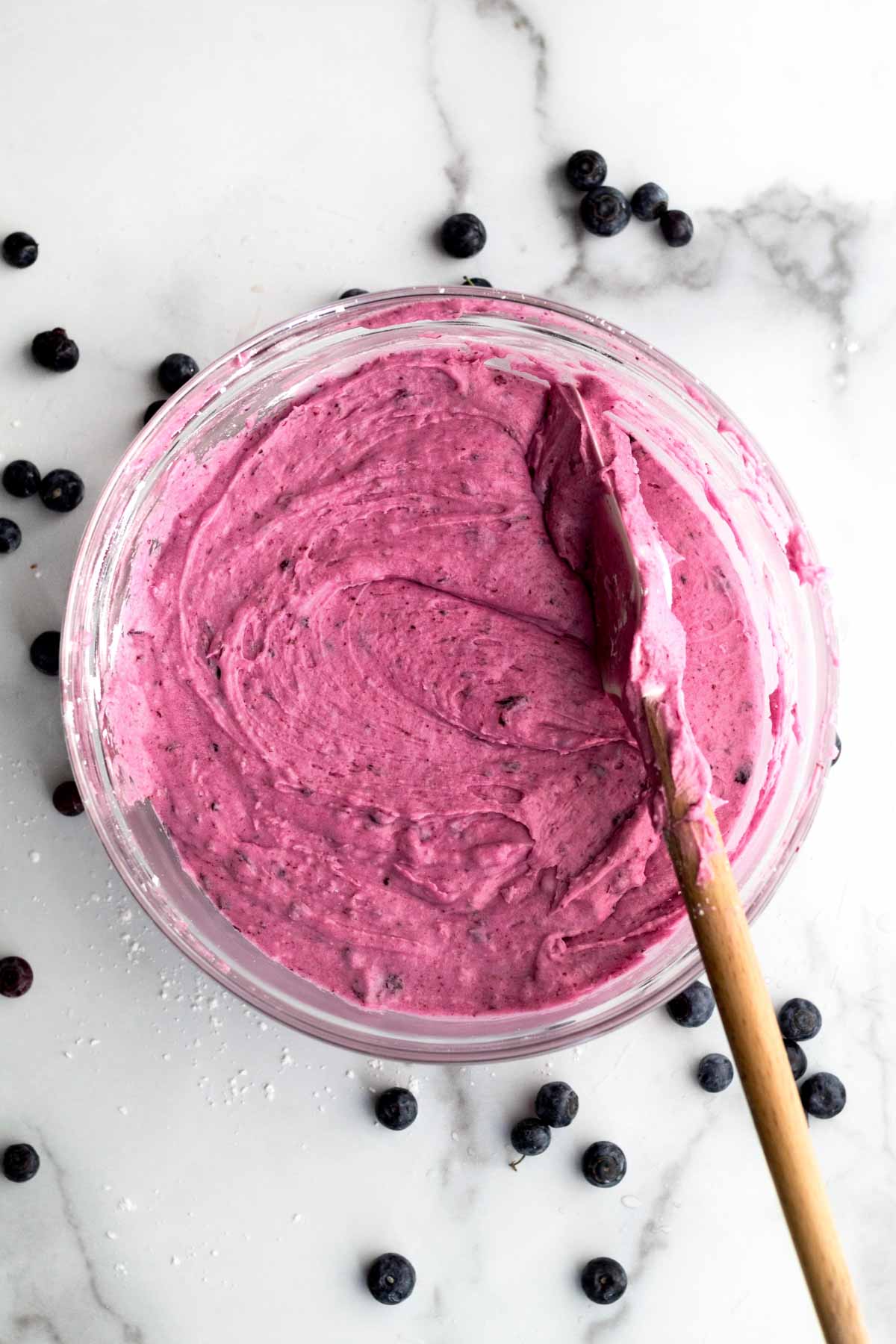 A bowl of creamy Blueberry frosting with a spatula.