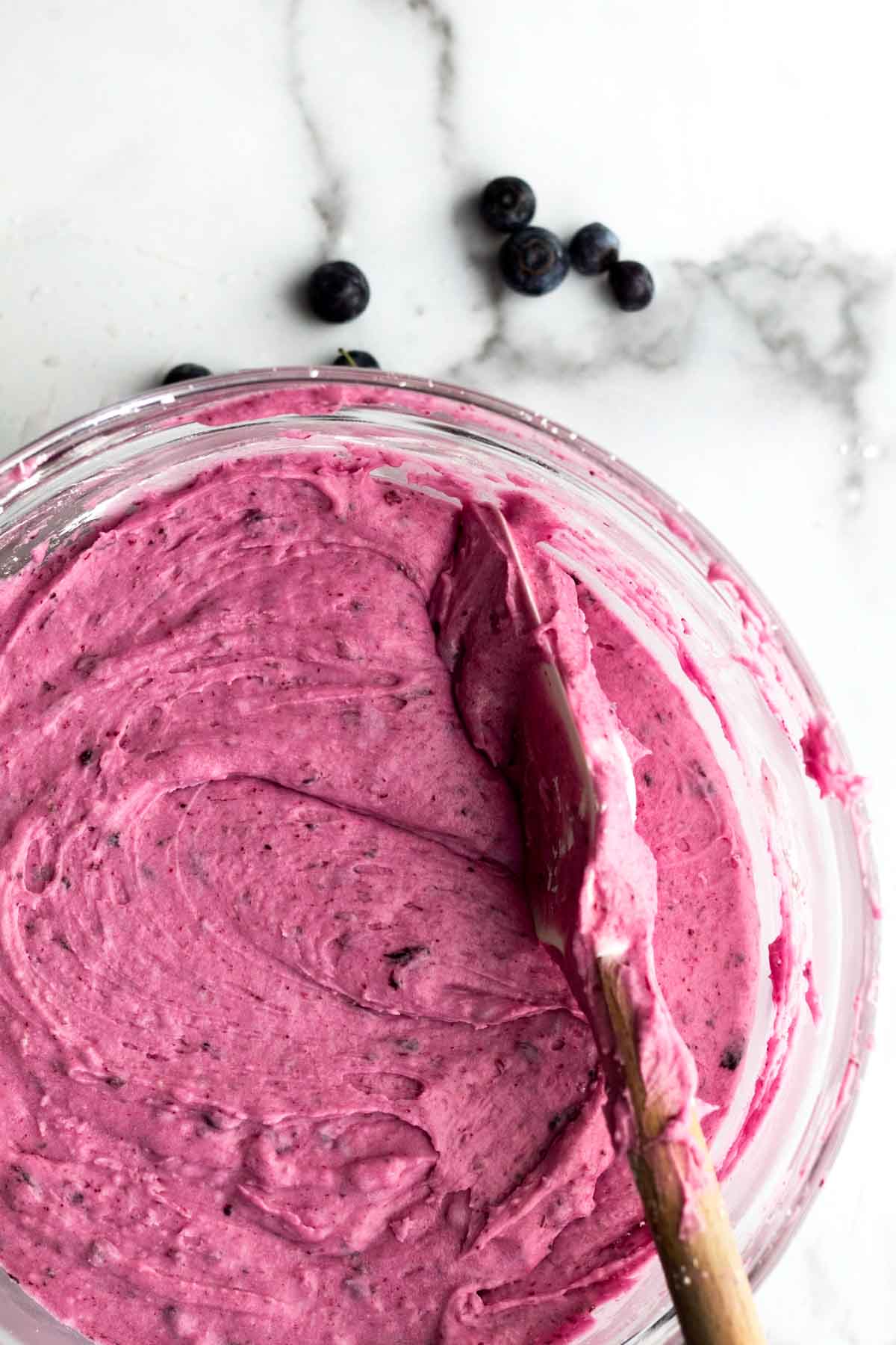 A bowl of creamy Blueberry frosting with a spatula.