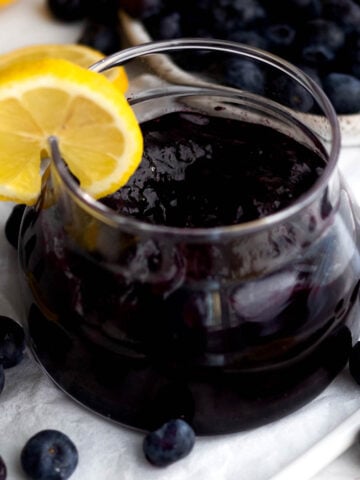 A glass ramekin with a lemon slice filled with Blueberry Jam.