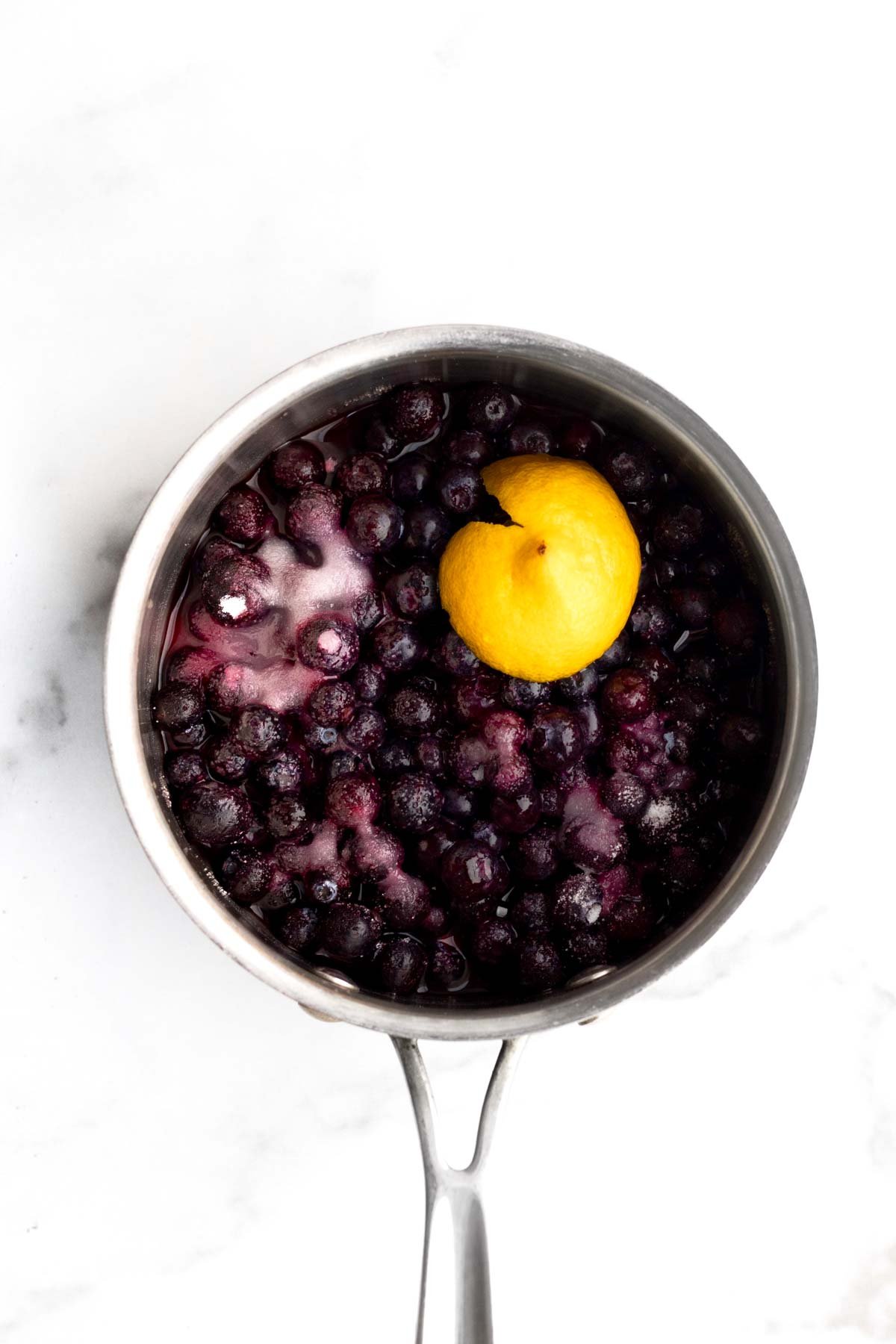 A saucepan with fresh blueberries, sugar and half a lemon.