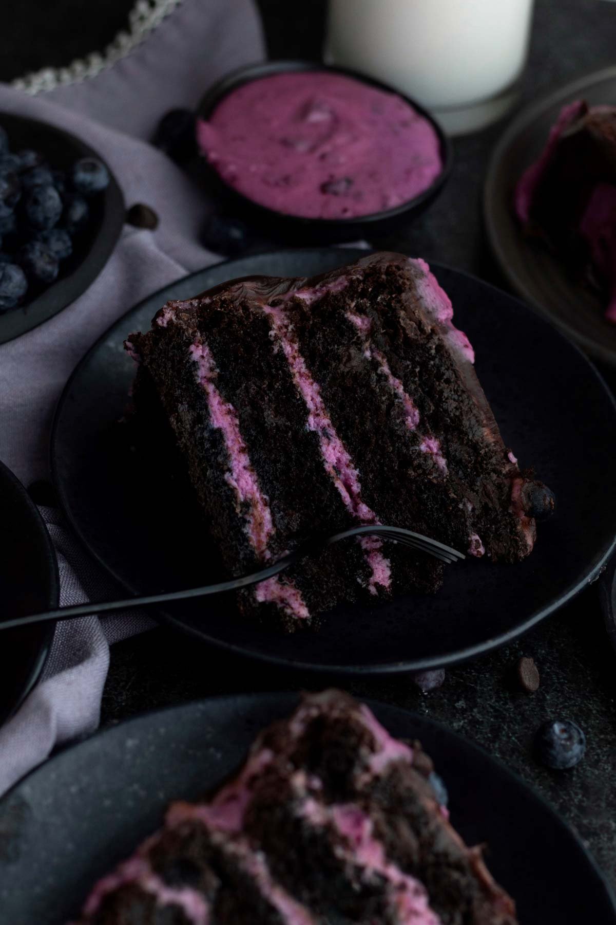 A fork slices into the dark chocolate cake with blueberry frosting.