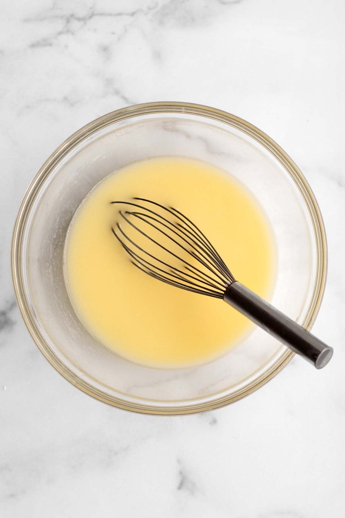 A yellow pool of heated butter in a bowl with a whisk.