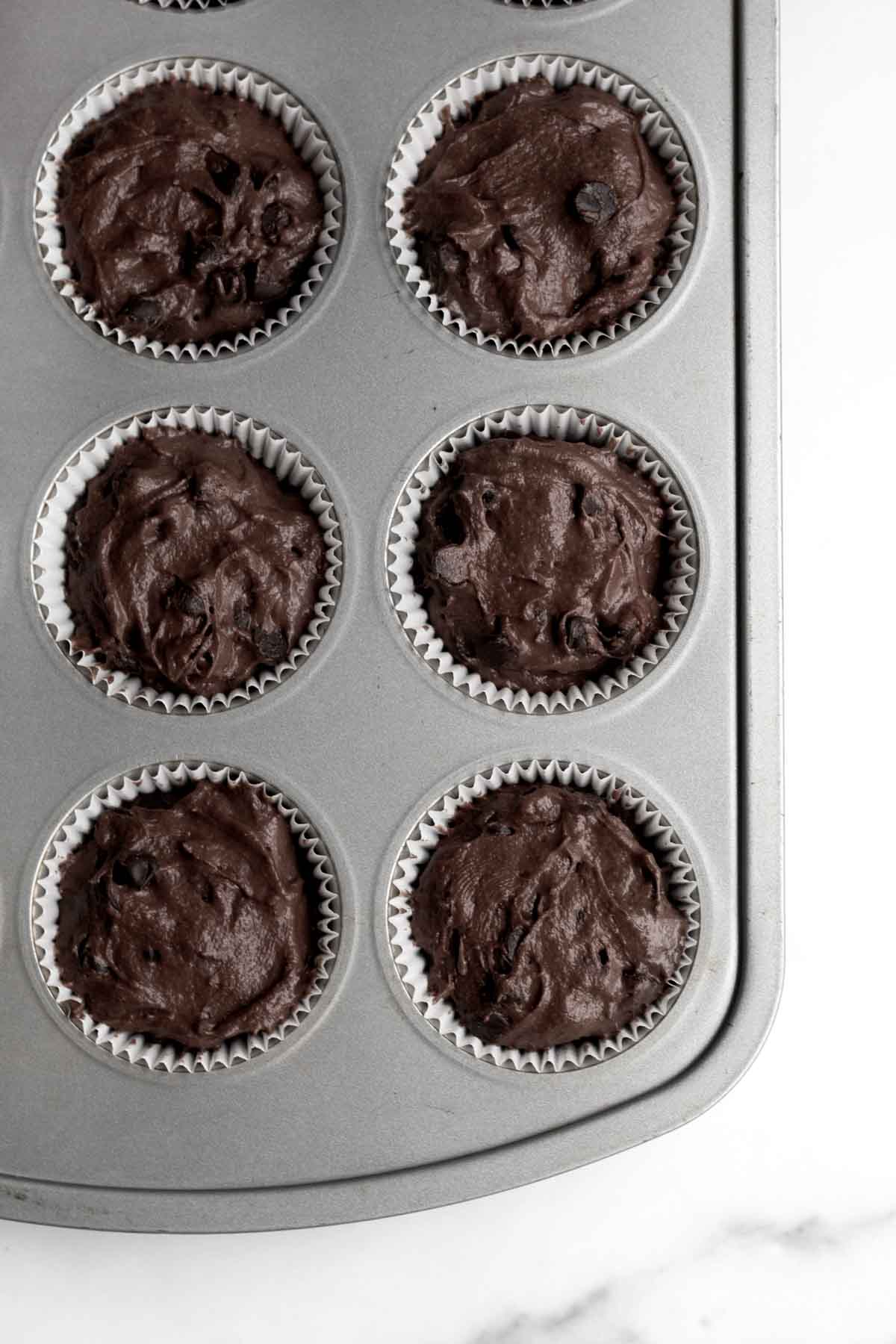 A muffin pan with the batter in muffin wrappers.