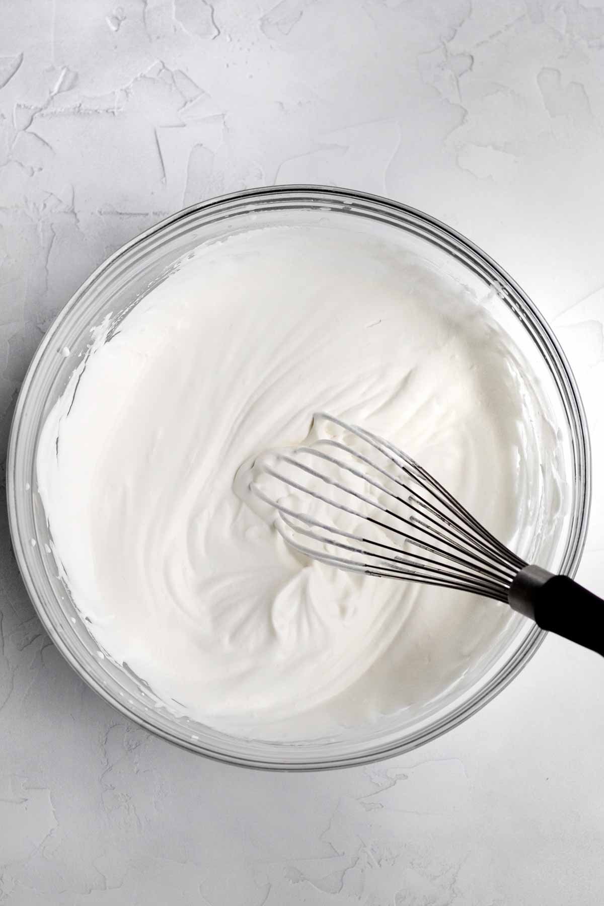 Heavy cream whipped with a whisk in a glass bowl.
