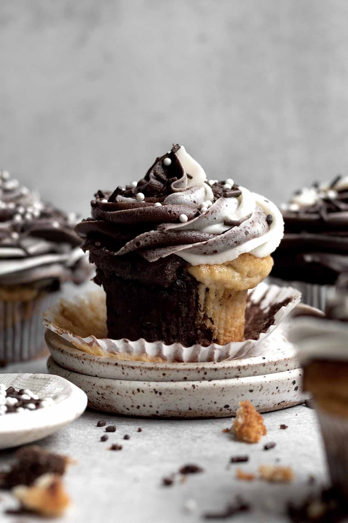 A Chocolate and Vanilla Cupcake with chocolate vanilla icing and round white sprinkles.