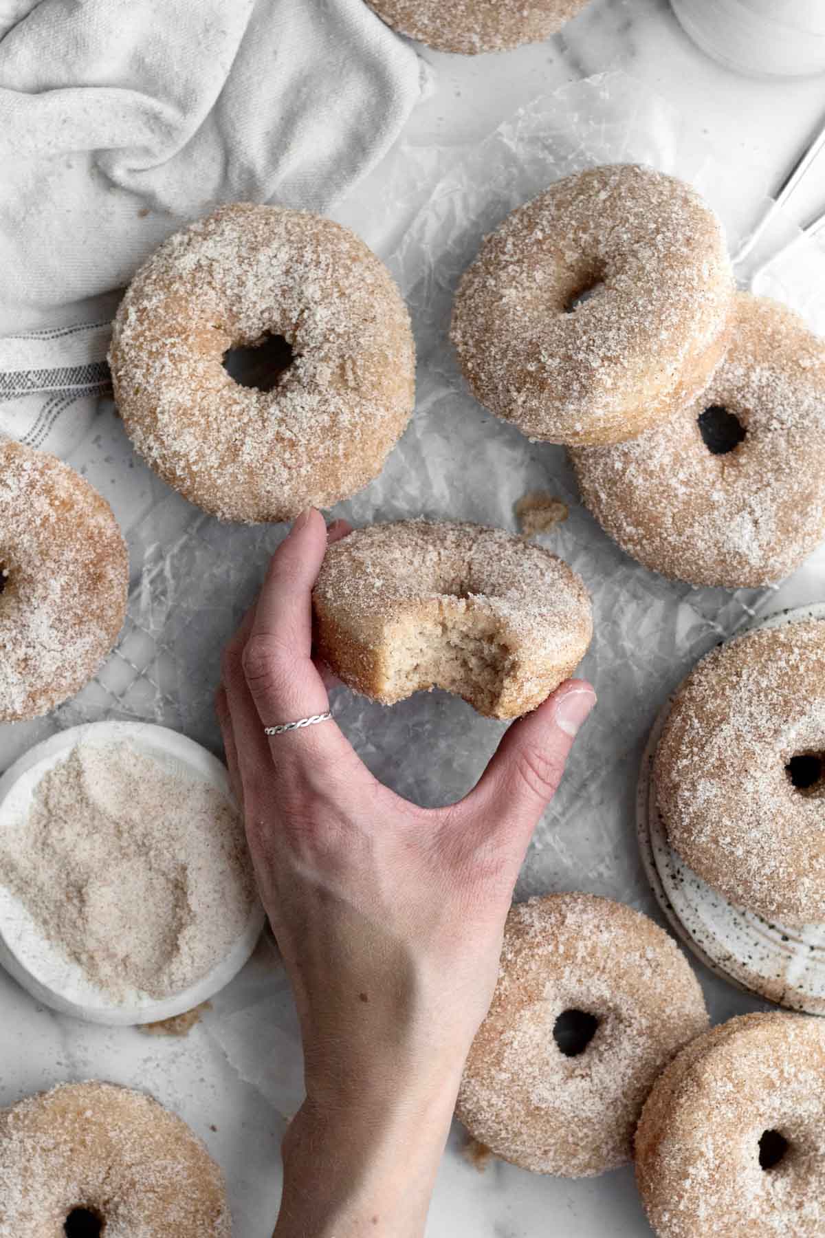 In a crowded table of donuts, a hand holds a bite one.