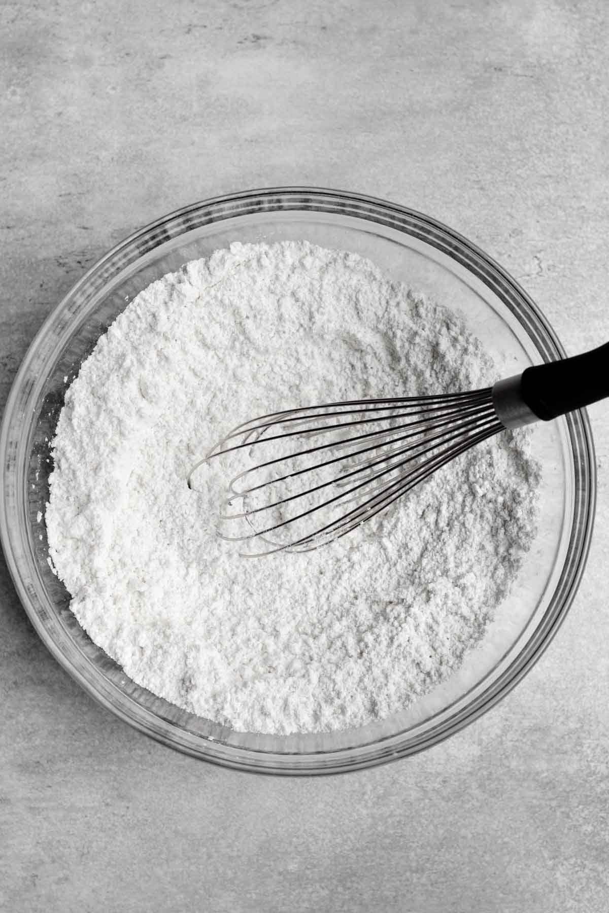 A whisk with the dry ingredients in a bowl.