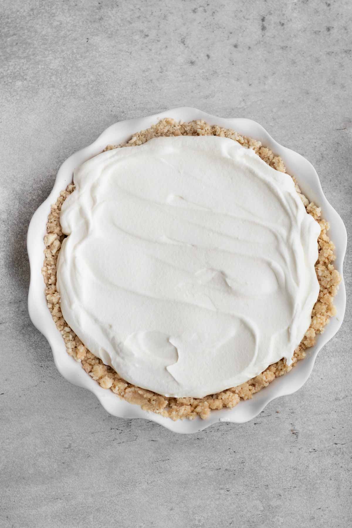 Putting a layer of whipped cream on top of the pie.