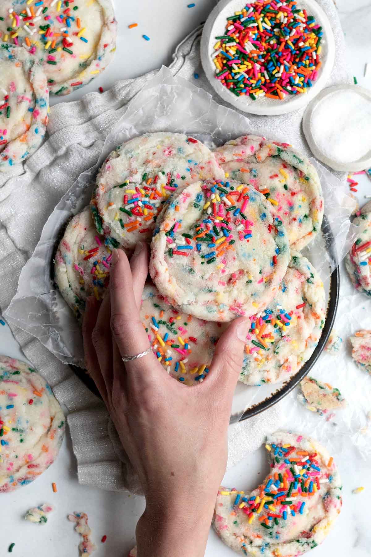 A hand reaches for a sugar cookie from a plate.