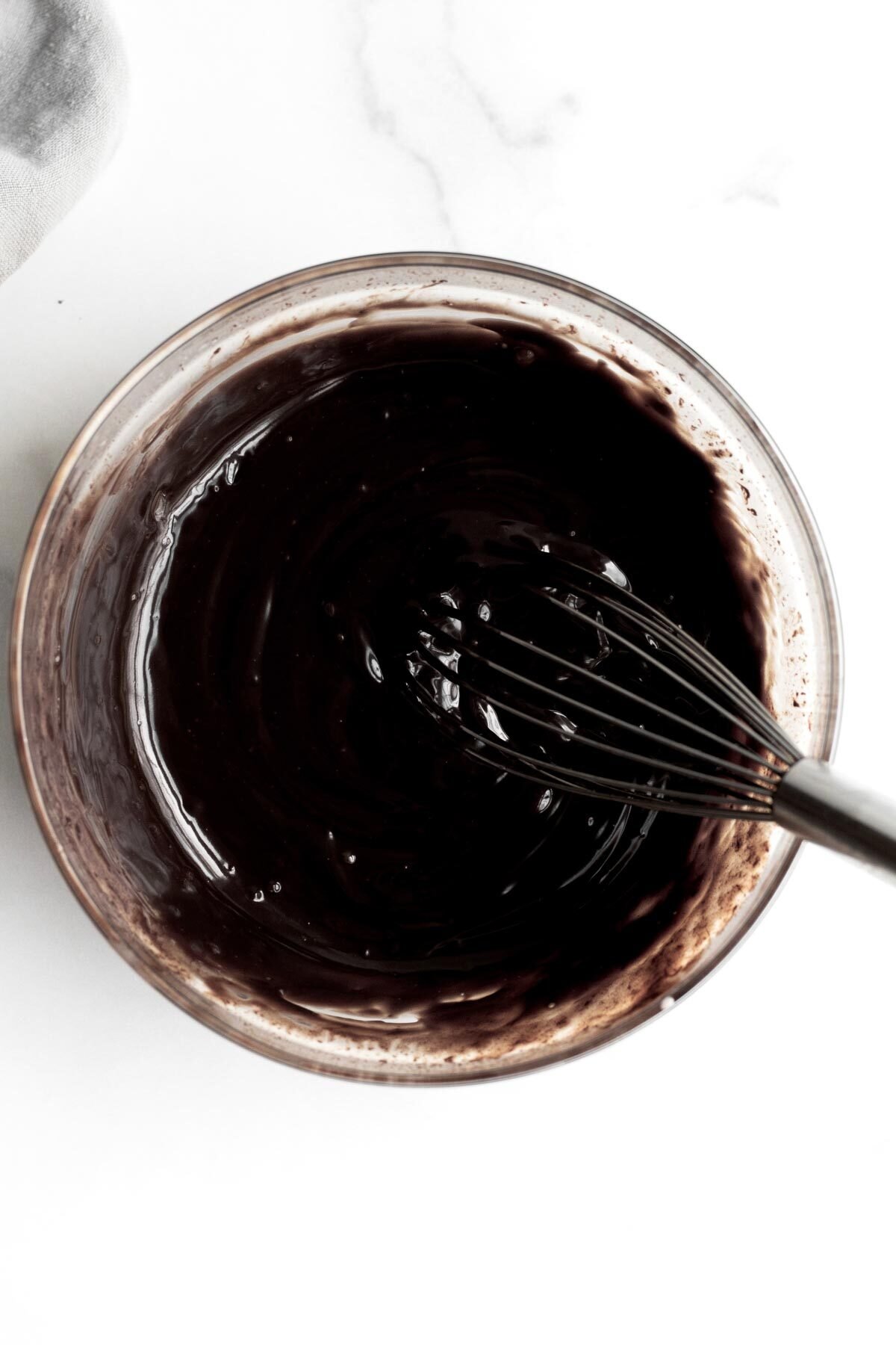 Warm chocolate ganache in a bowl with a whisk.