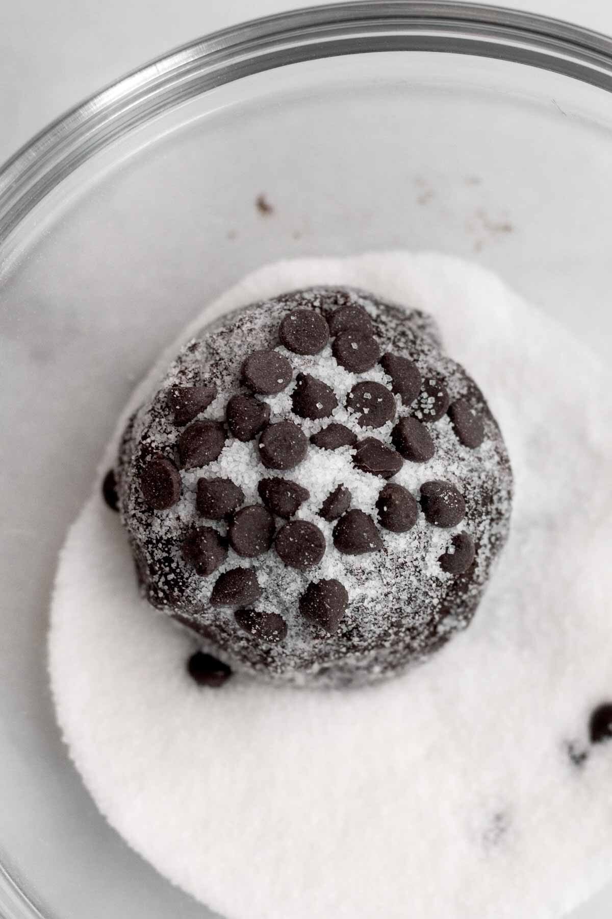 A dough ball with chocolate chips in a bowl of sugar.