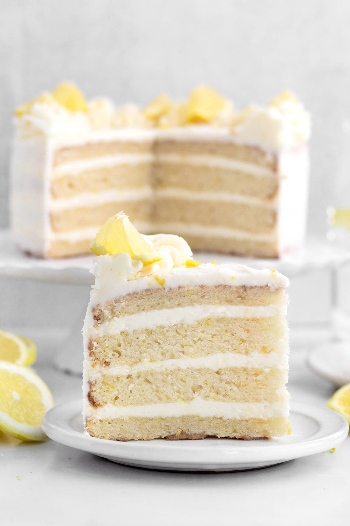 Slice of lemon cake in the foreground with the whole behind it.