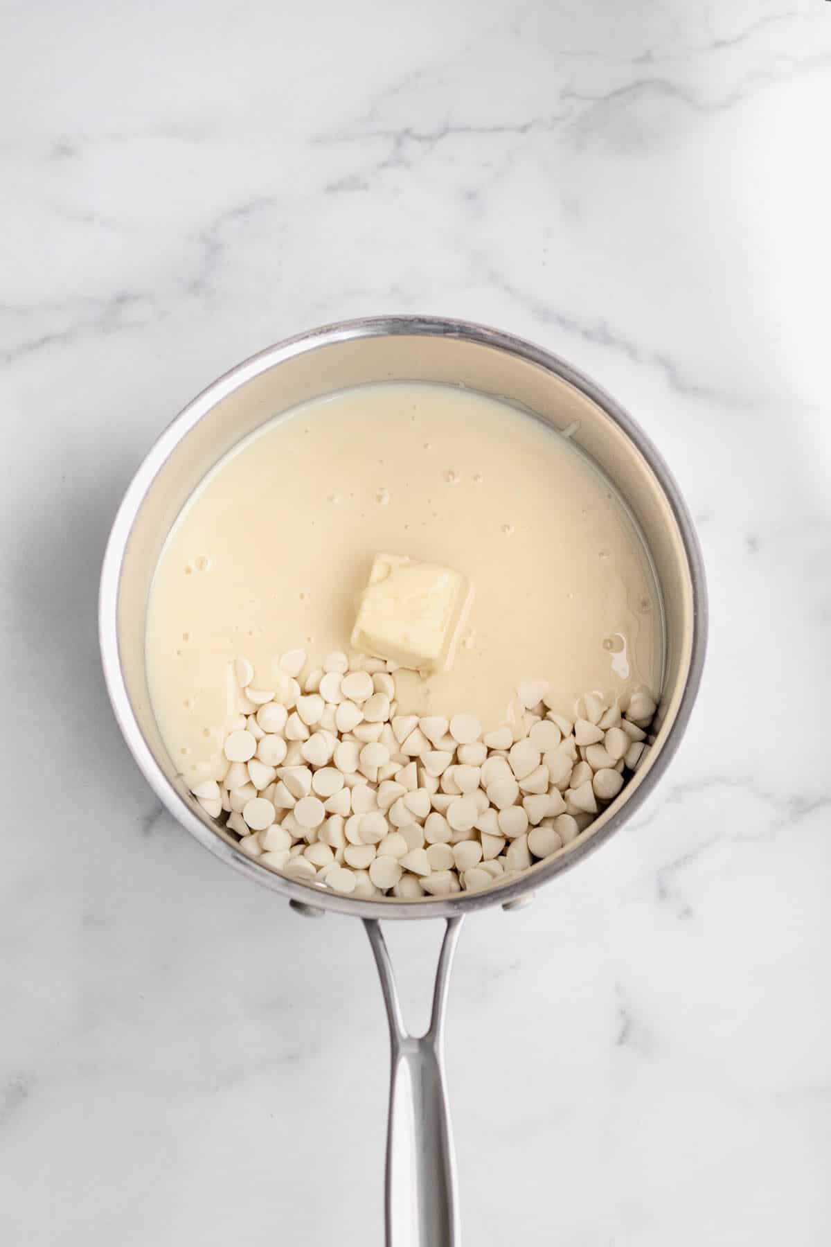 A saucepan with white chocolate chips, butter and condensed milk.