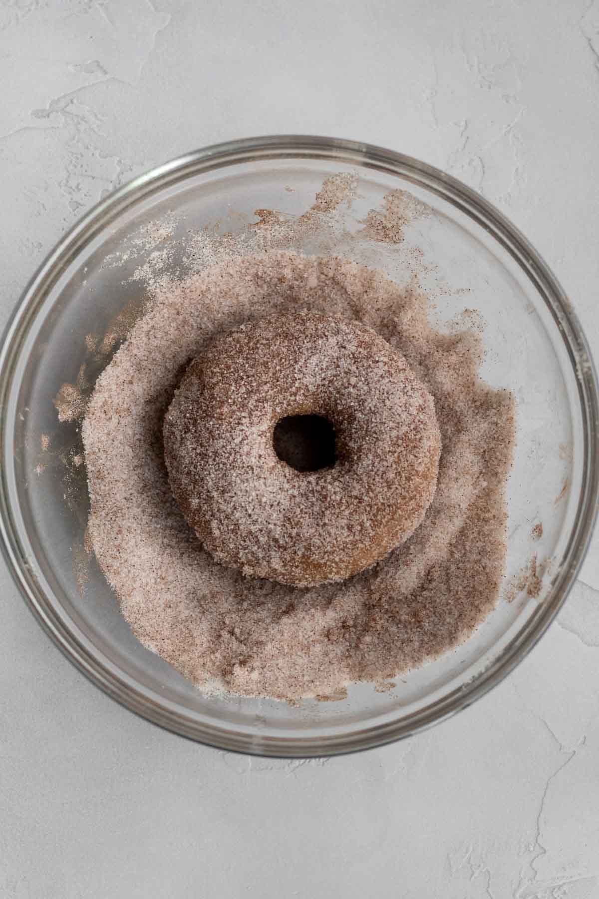 Covering the donut with cinnamon sugar.