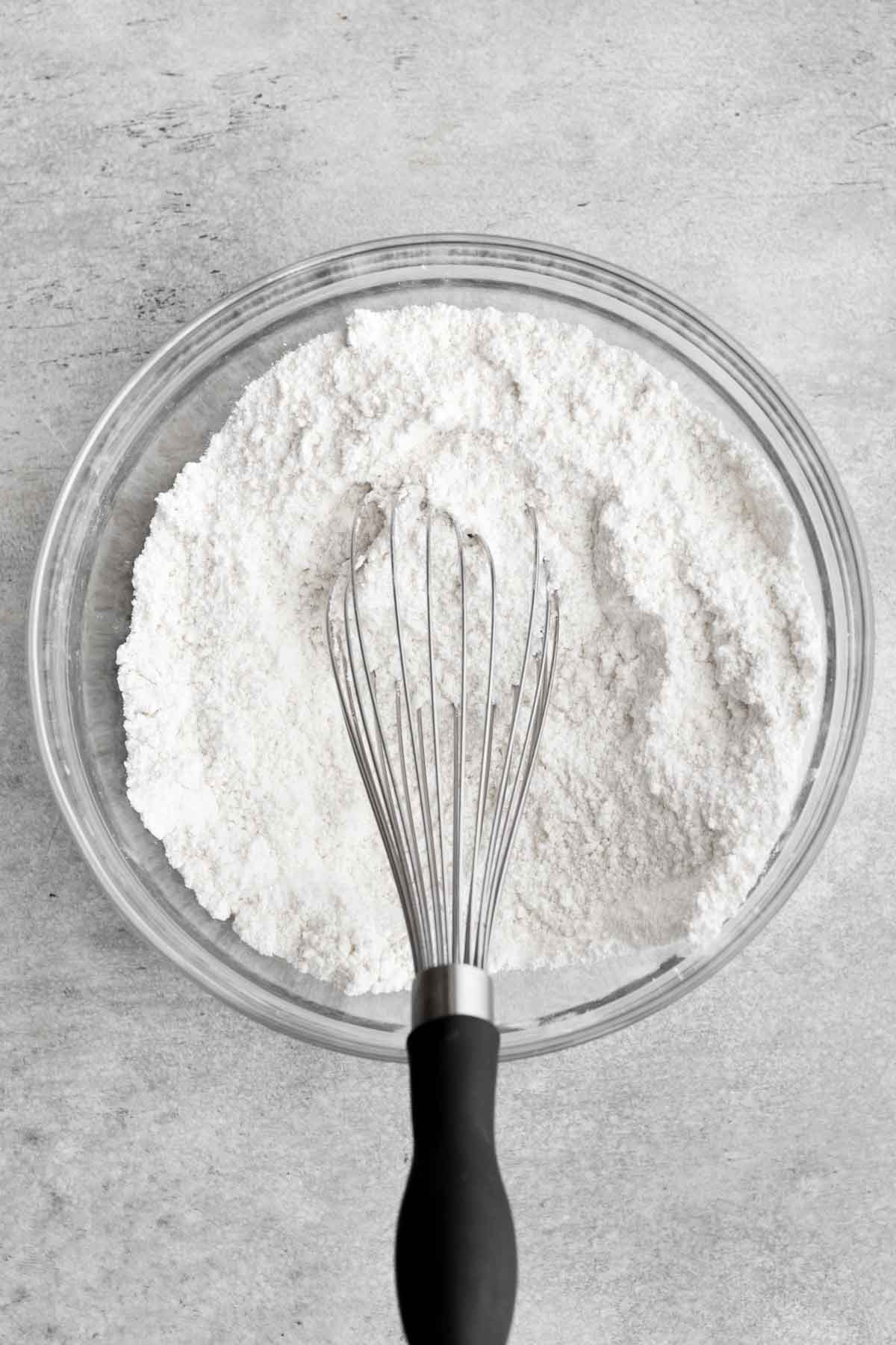 A whisk with the white dry ingredients in a bowl.