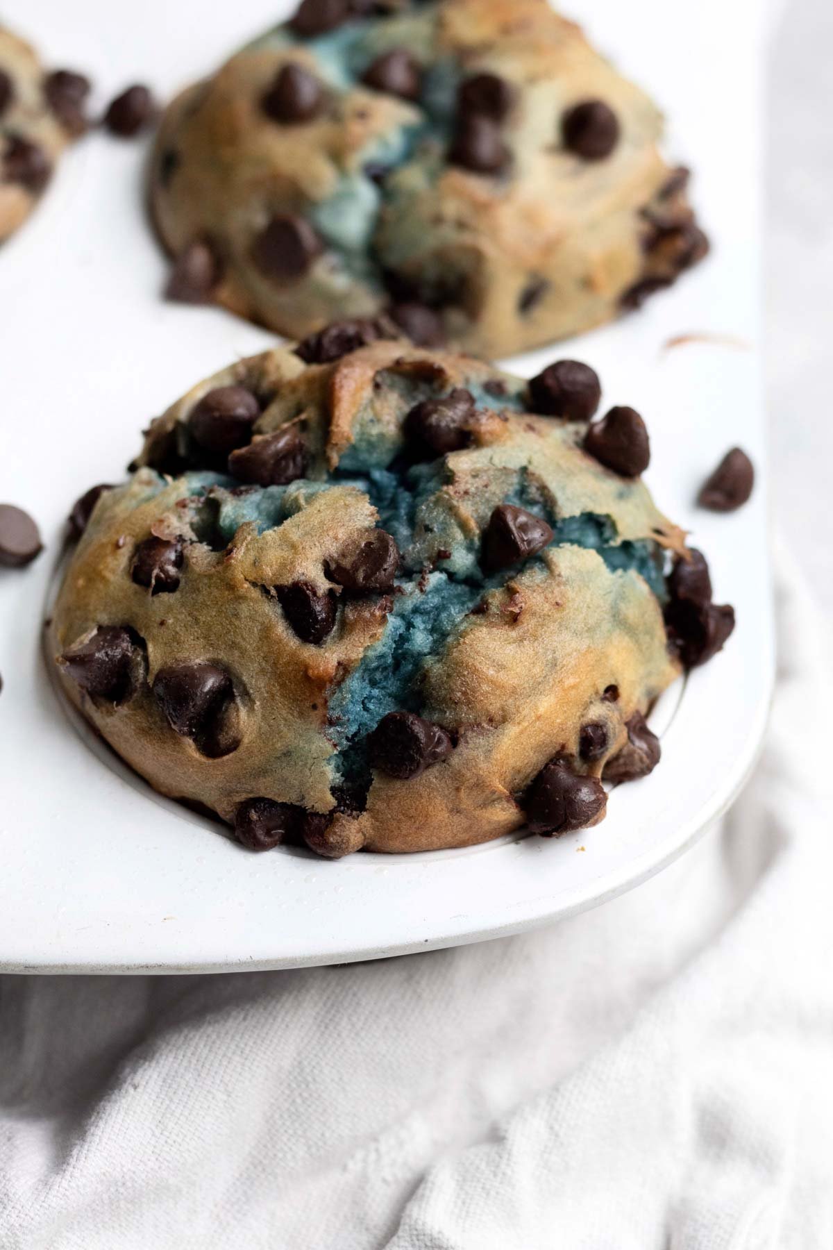 Gluten free muffins in a tin with blue cracks from the blueberries.