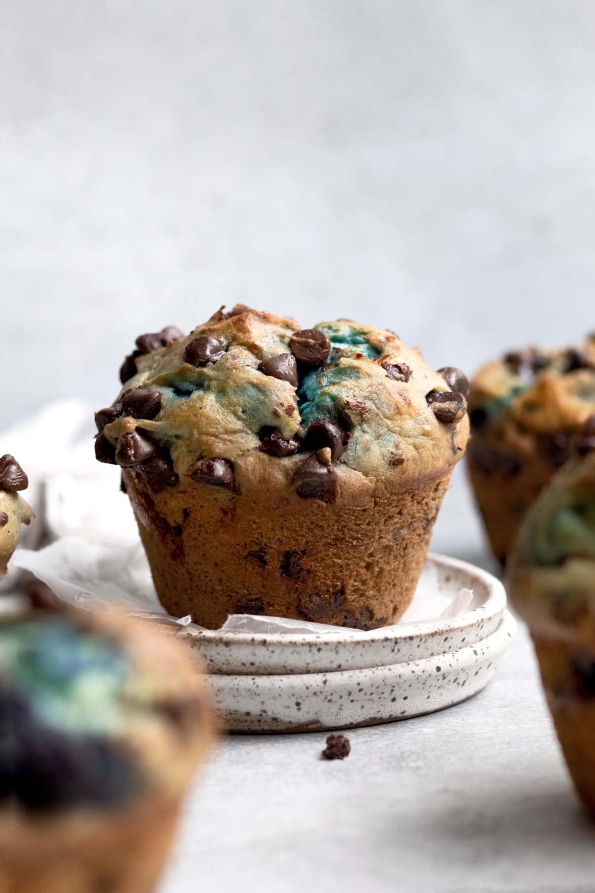 Golden brown chocolate chip muffin with blue streaks stands peacefully on a plate.