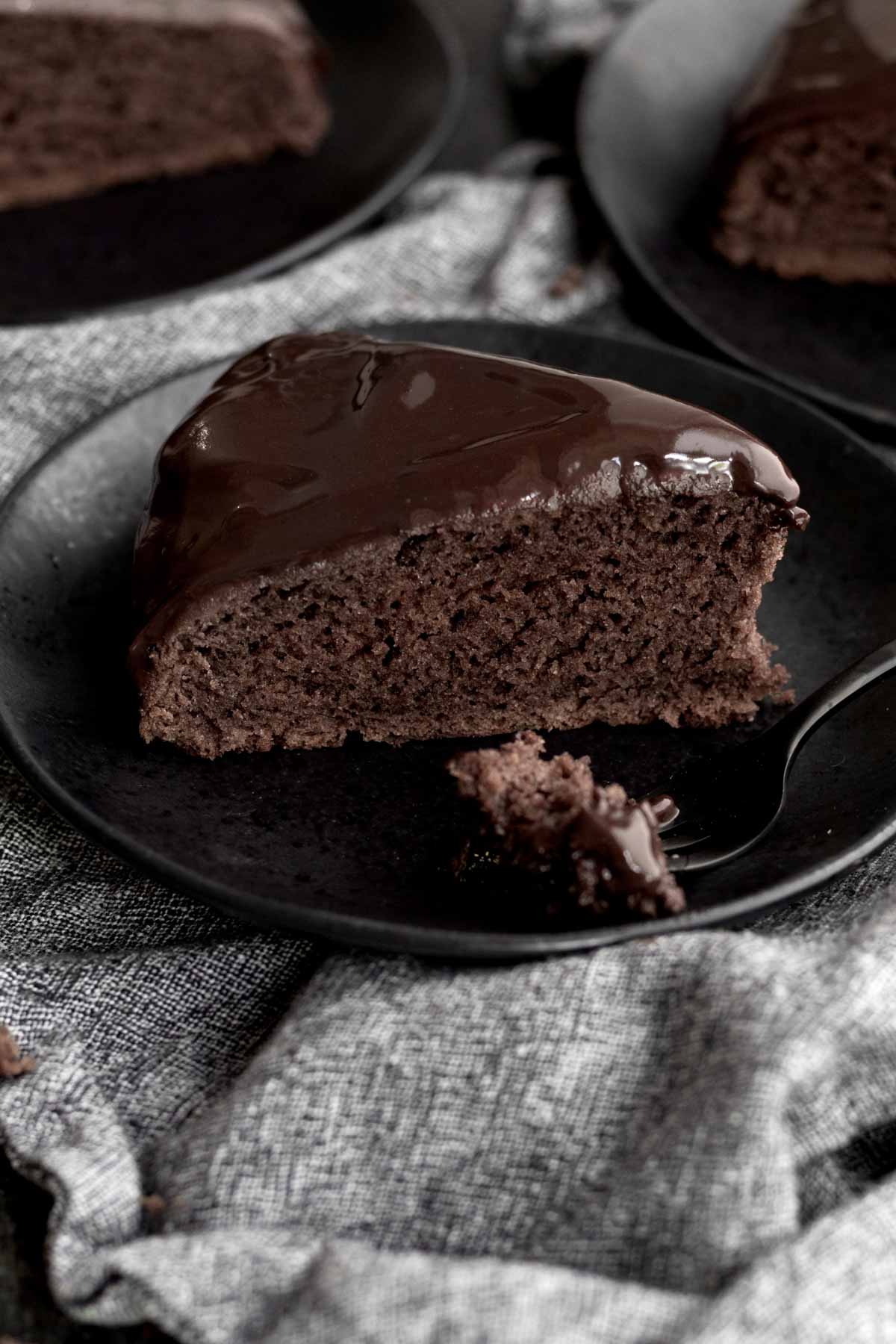 A slice of chocolate glazed cake on a plate with a fork.