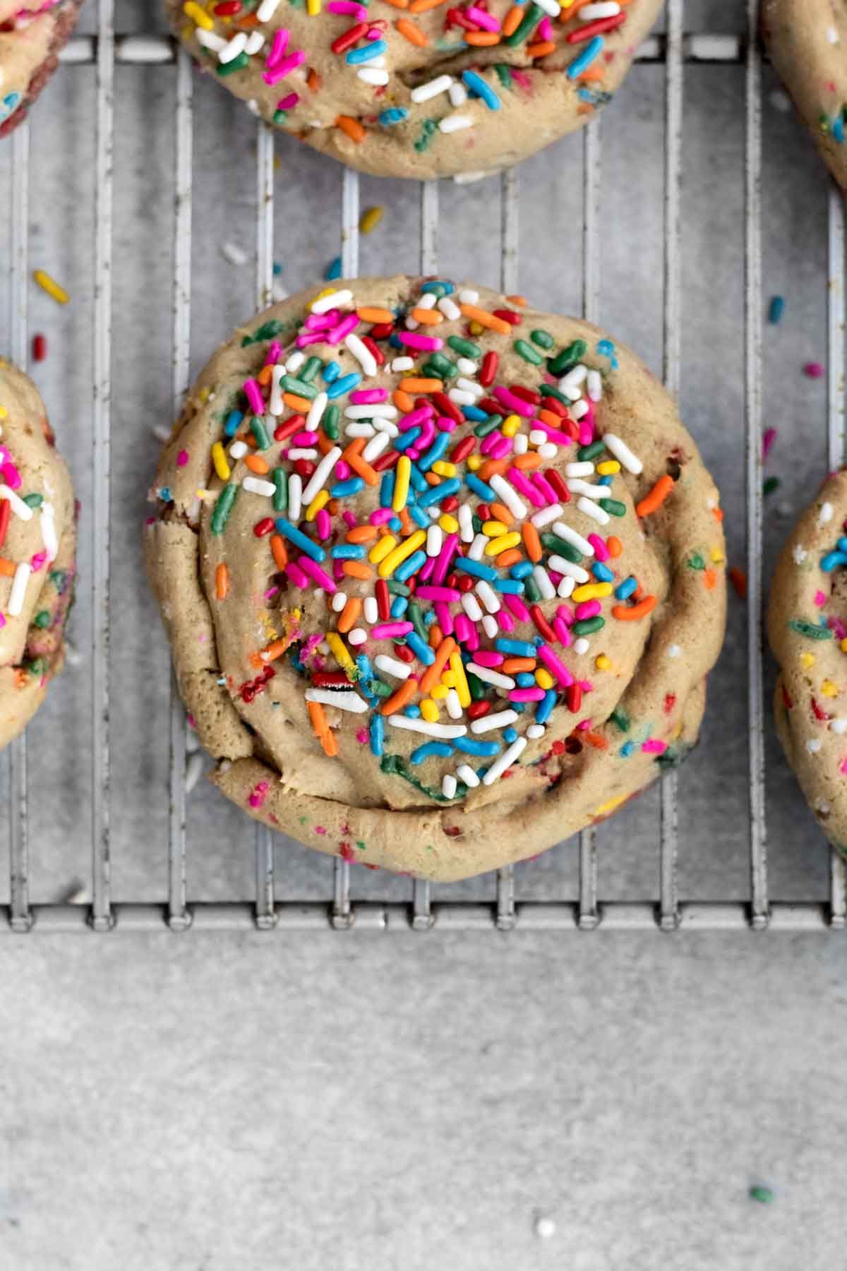 A rainbow sprinkled Funfetti Cookie on a cooling rack.