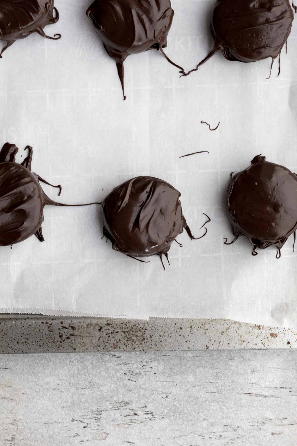 Oreos covered in chocolate on parchment paper.