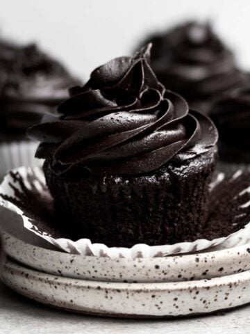 A stout chocolate cupcake with chocolate frosting with the wrapper pulled down.