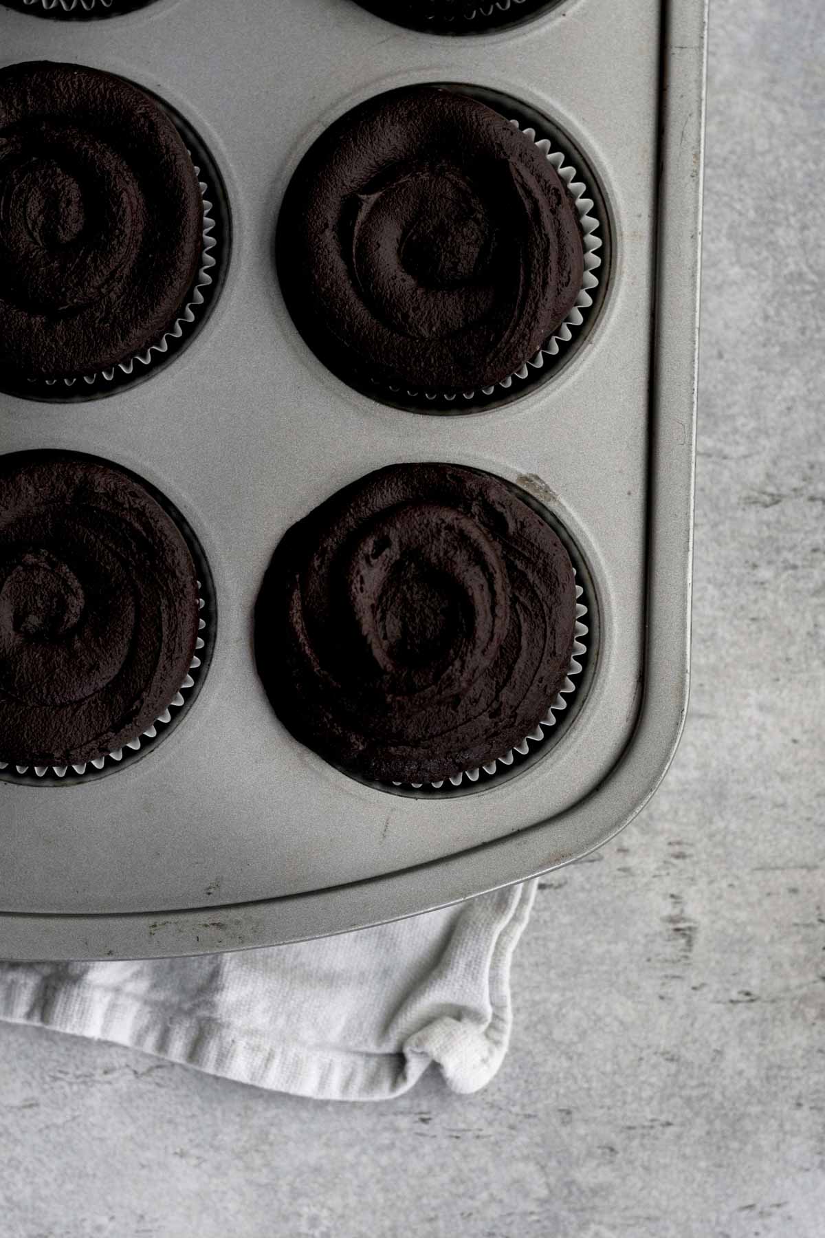 Chocolate frosted cupcakes in a cupcake tin.
