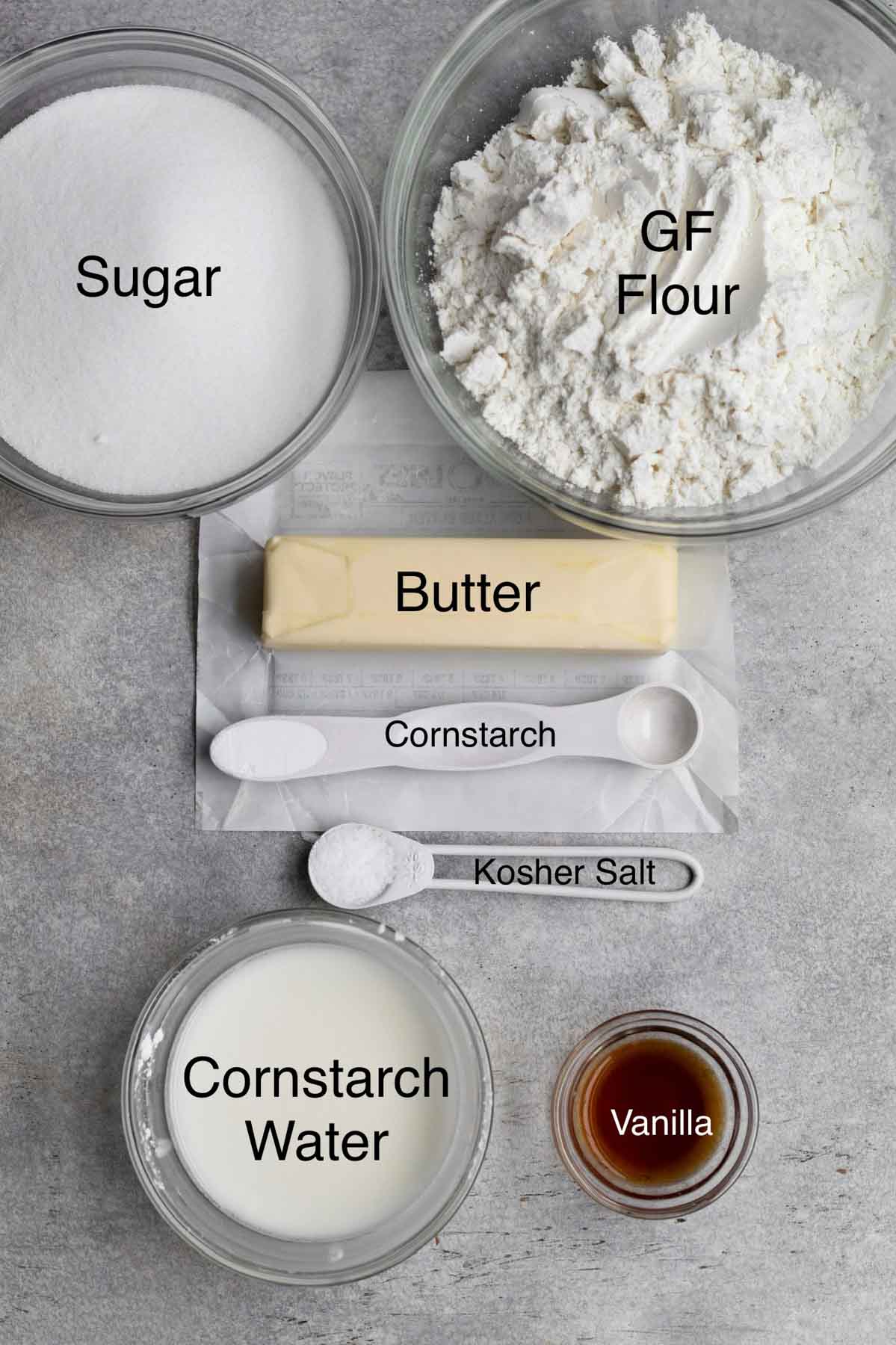 The ingredients for the sugar cookies in separate containers with their text names.