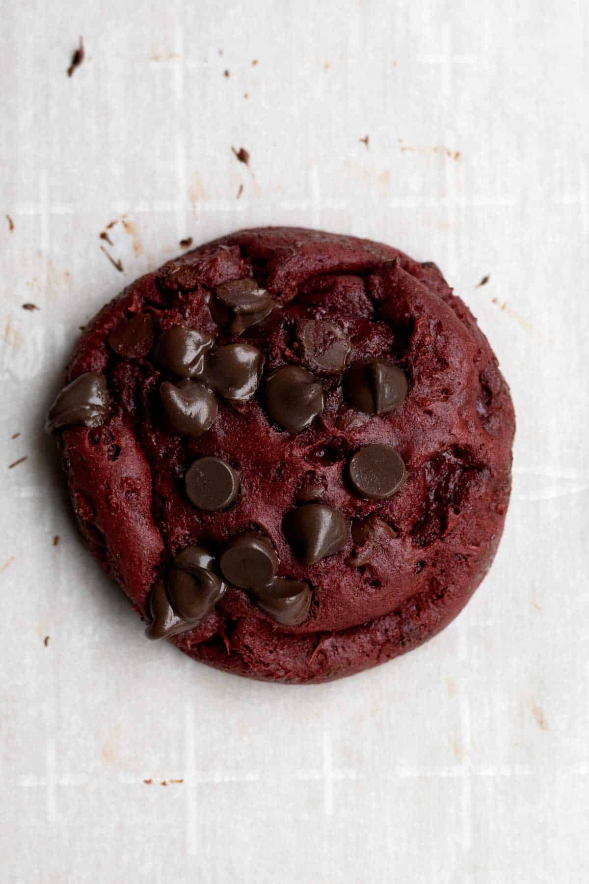 A hot cookie with melted chocolate chips on wax paper.